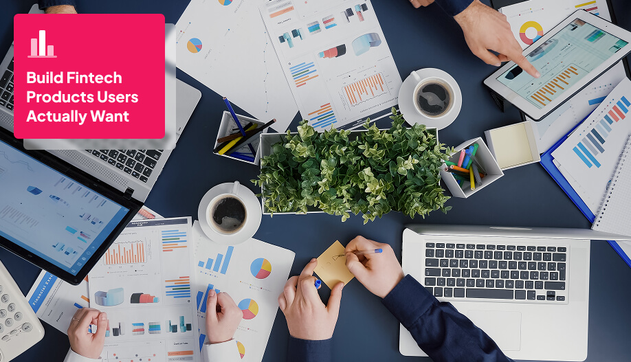 desk with laptops, coffees, pens, and papers with people working together